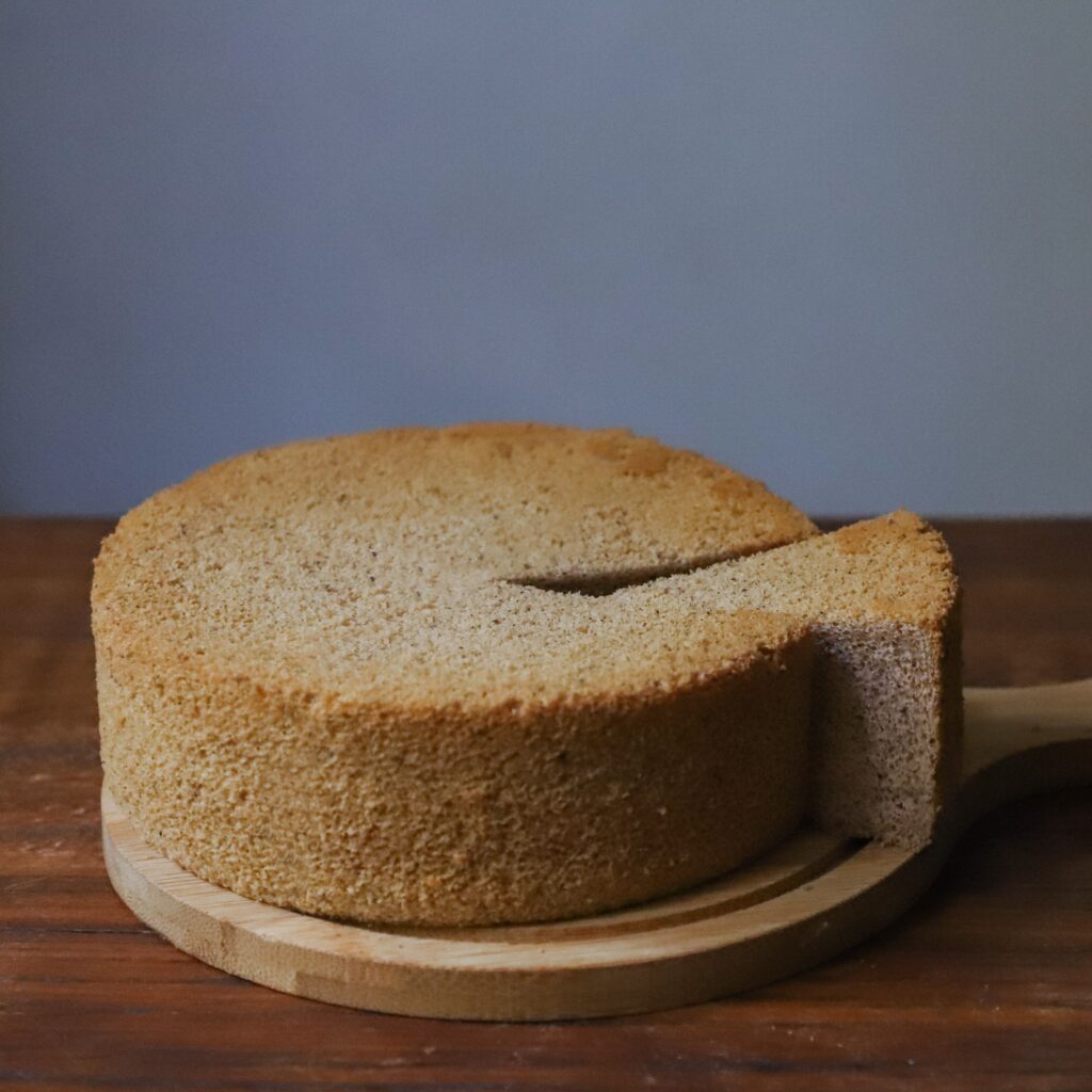 A freshly baked sponge cake with a slice cut out, presented on a wooden board.
